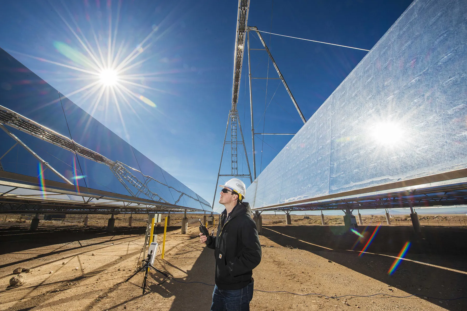 Engineer standing between polished solar thermal reflectors in a desert solar field.
